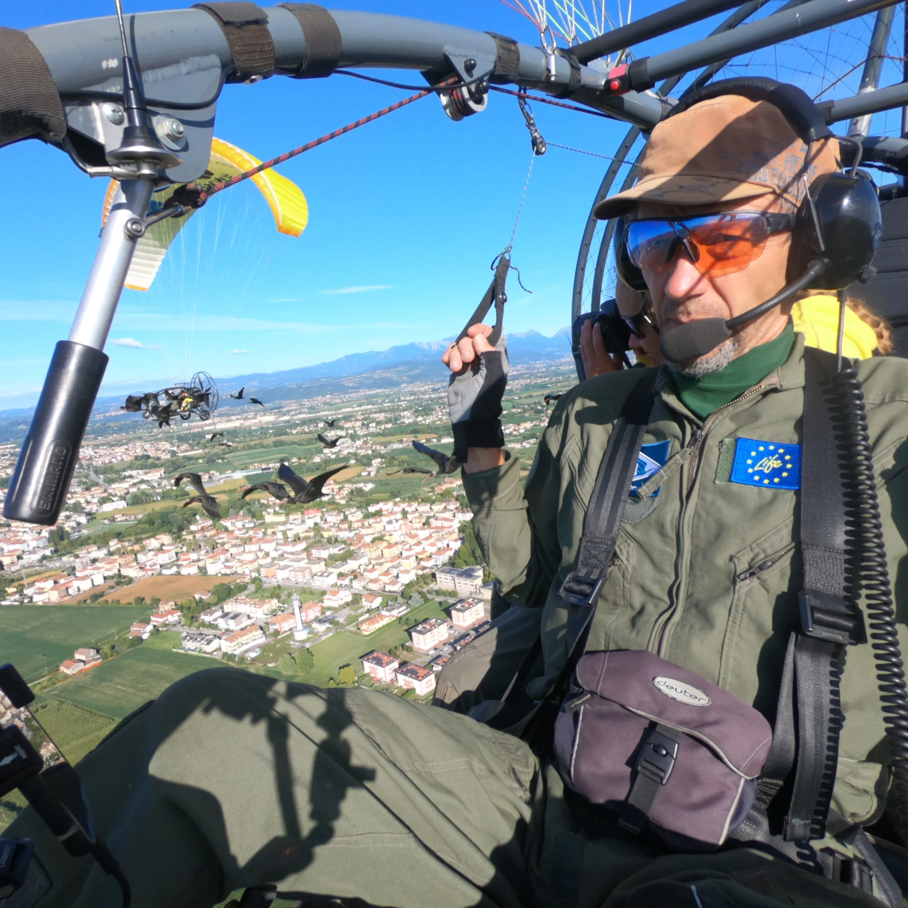 Portrait von Johannes Fritz hoch über dem BOden, im Hintergrund ein Waldrappschwarum und eine weitere fliegende Begleitperson